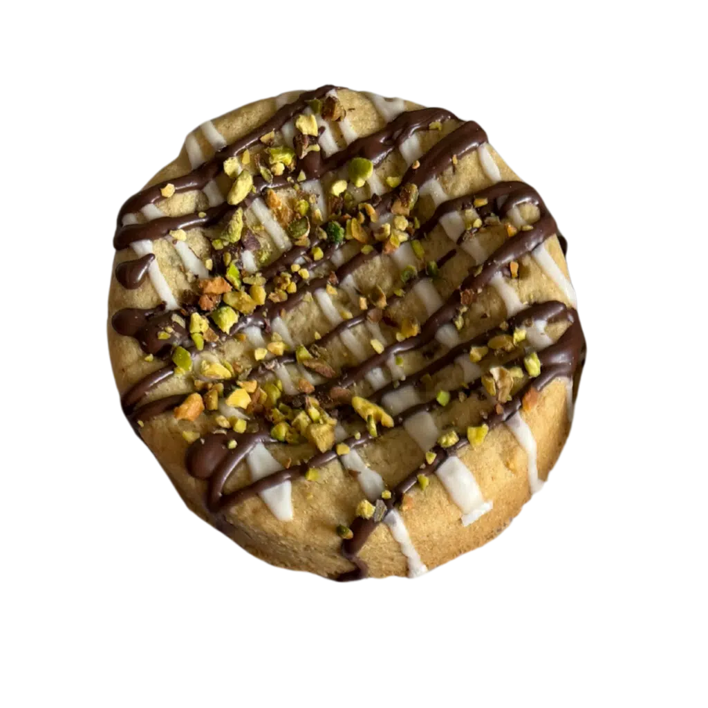 A thick, gourmet gluten-free cookie topped with a white chocolate base, a dark chocolate drizzle, and a generous sprinkle of crushed pistachios.