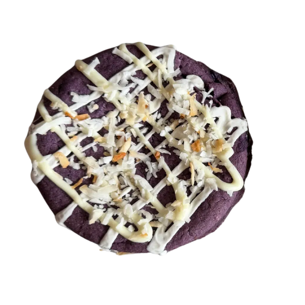 A thick gourmet gluten-free Ube cookie with a vibrant purple center, topped with a white chocolate drizzle and toasted coconut flakes.
